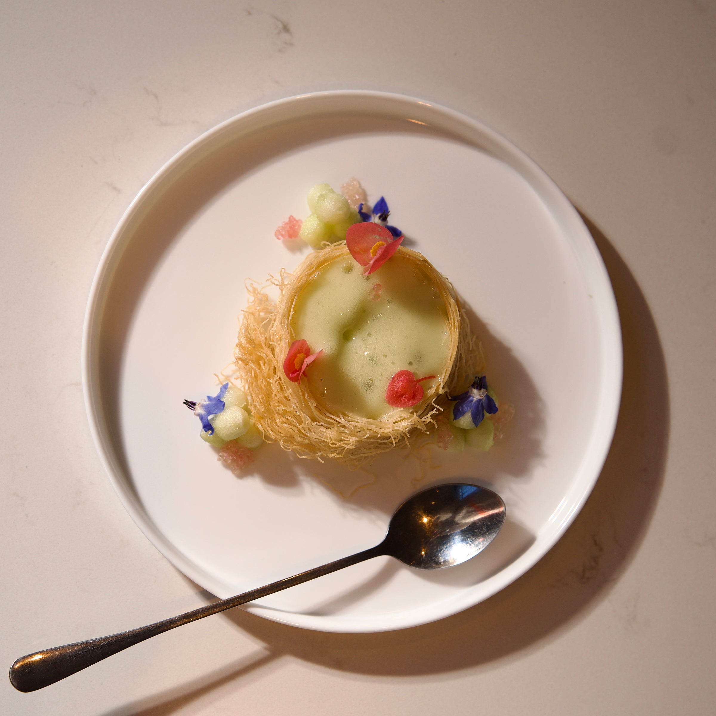 Small dessert in a nest with flowers on a white dessert plate with a spoon