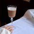 Glass of fall cocktail held by a hand on a white surface with a dark background