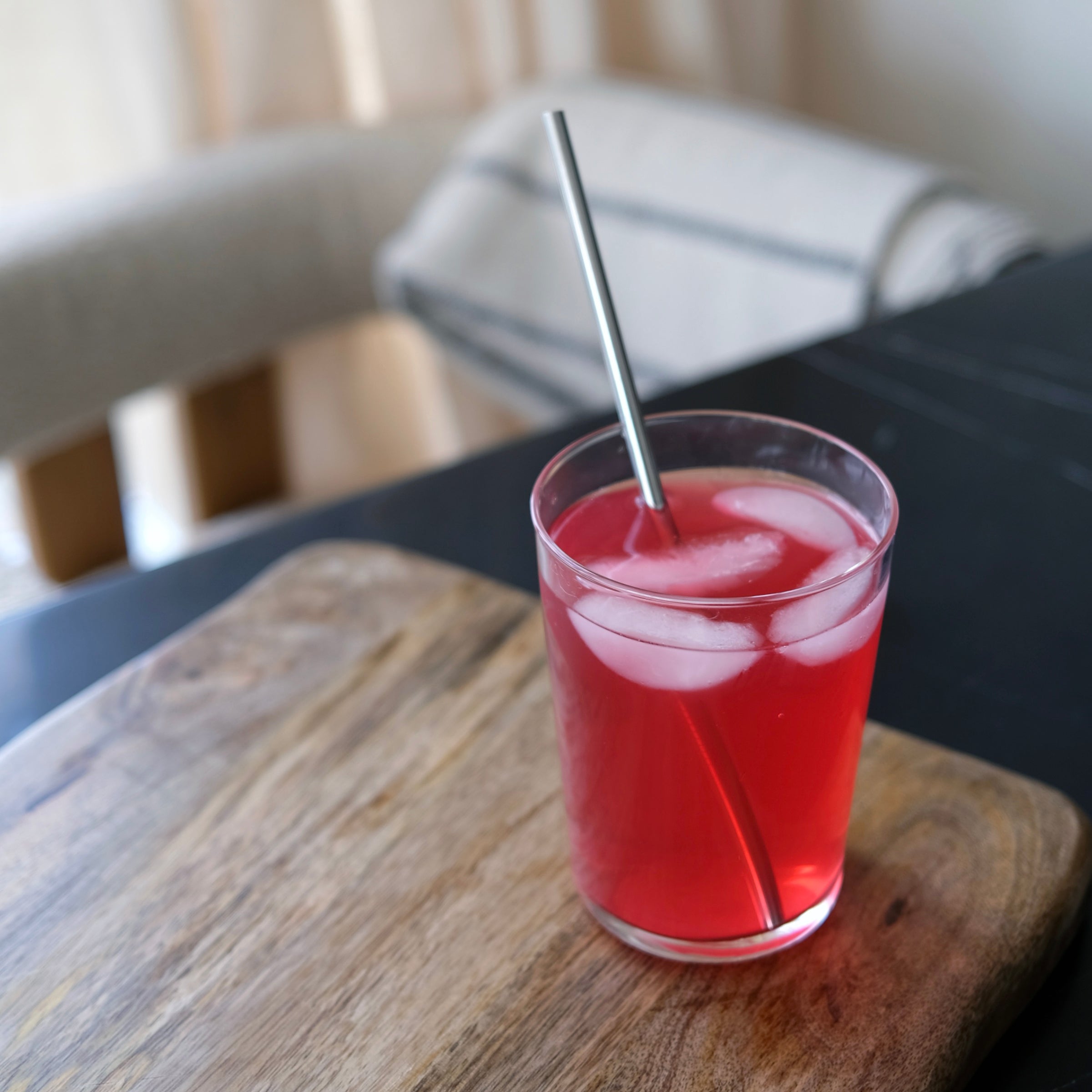 Glass of red drink with ice and a straw on a wooden table.