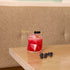 Red cocktail with ice and blueberries in a Cassiopea DOF glass, on a wooden table against a beige wall.