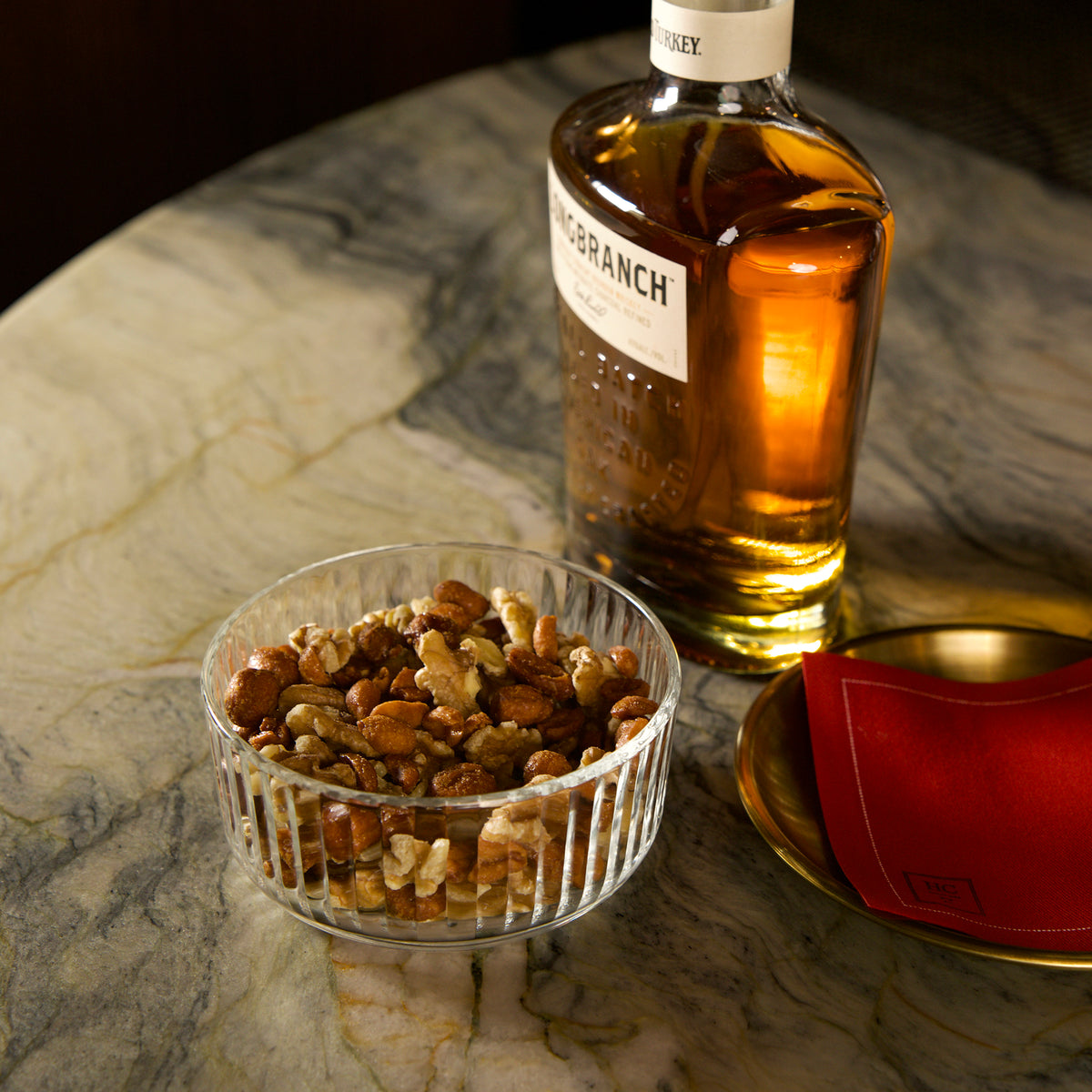 Bottle of whiskey and Exclusiva bowl of nuts on a marble table.