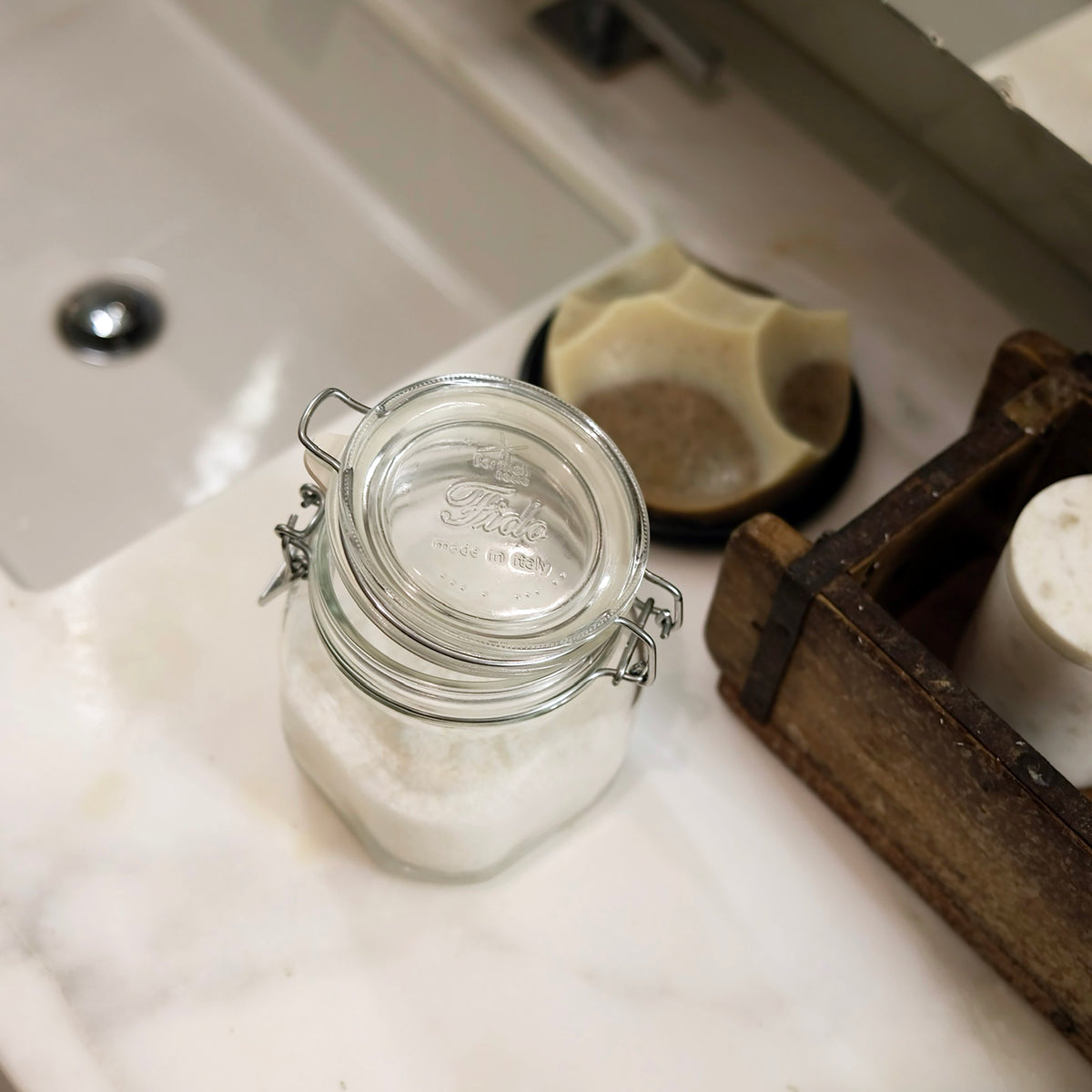Glass jar with a metal clasp on a bathroom counter next to a soap dish with a bar of soap.