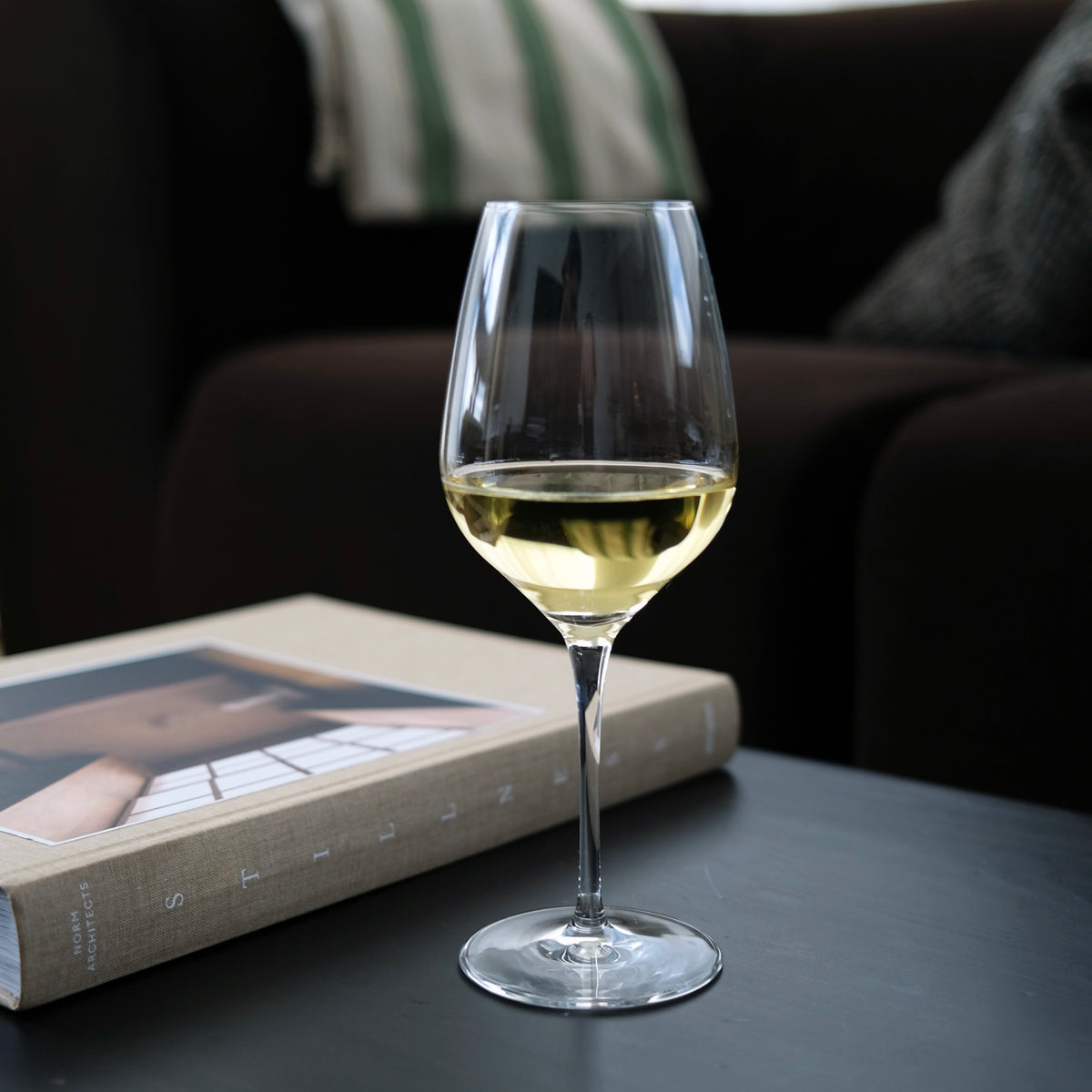 Wine glass with white wine on a table next to a book, with a blurred background