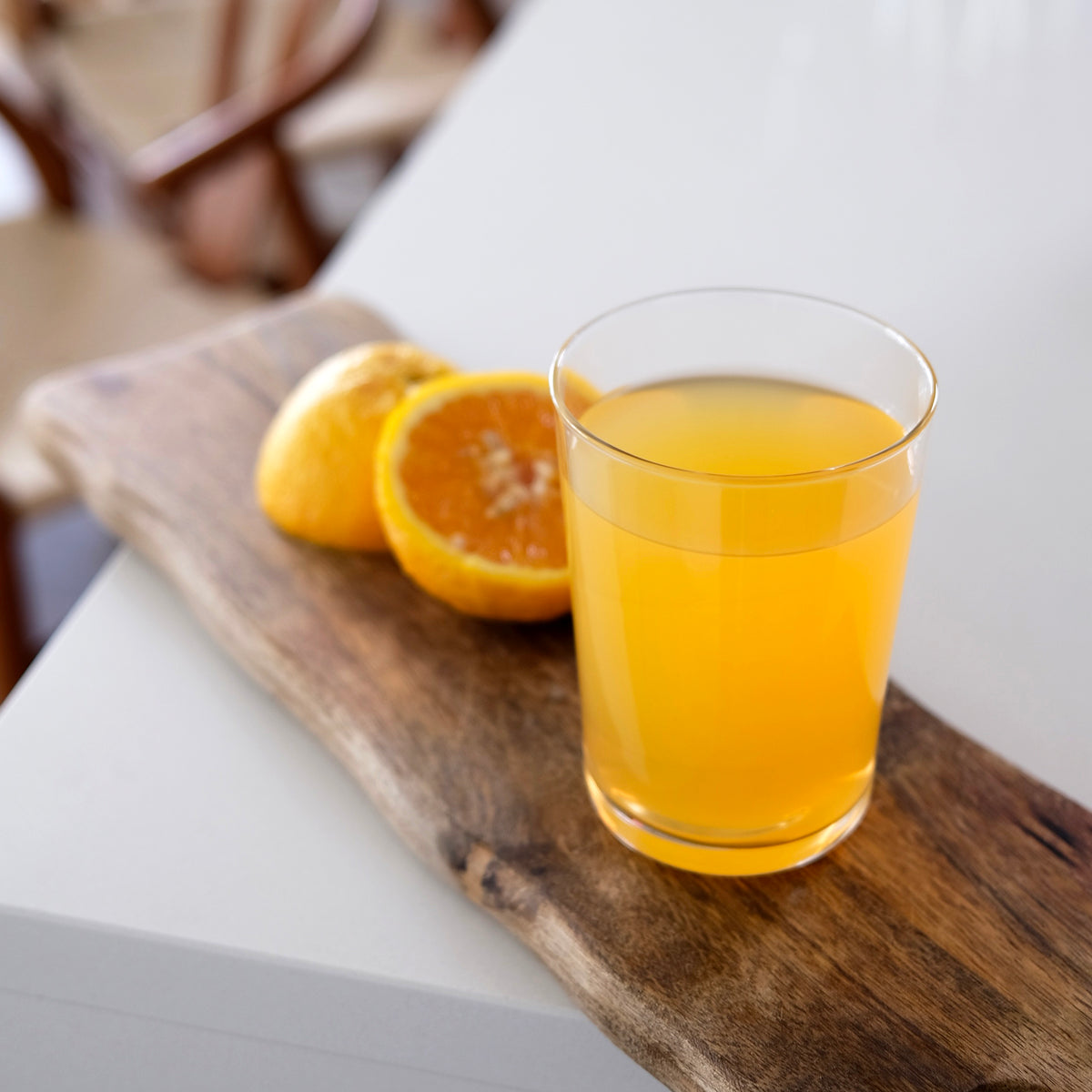 Glass of orange juice on a wooden board with oranges in the background